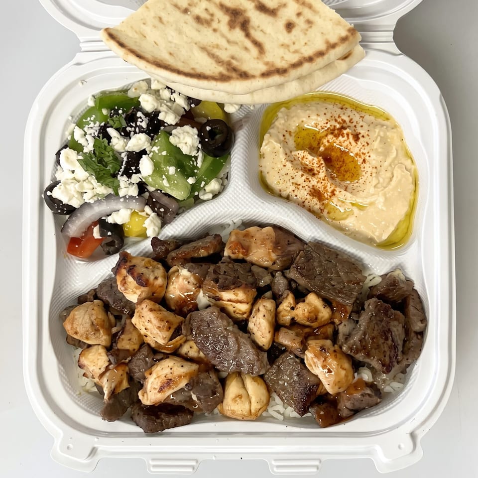 Mediterranean platter with grilled chicken and beef, pita bread, hummus, Greek salad, and rice.