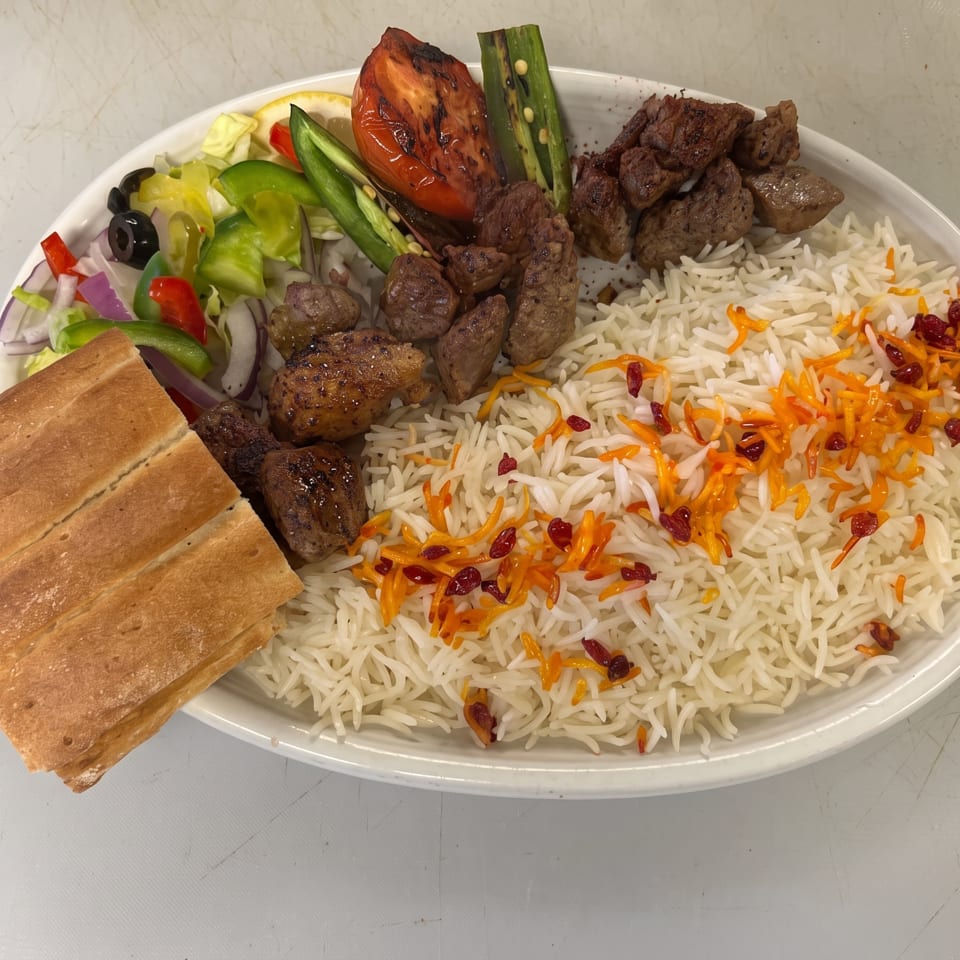 Platter of saffron basmati rice with grilled beef, roasted vegetables, salad, and flatbread.