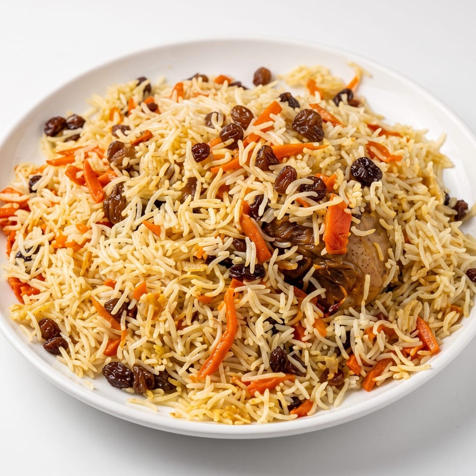 Plate of spiced rice pilaf with carrots, raisins, and browned meat pieces.